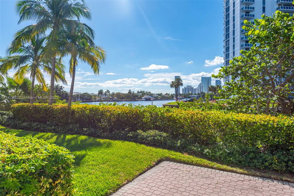 View of tall residential buildings near water with palm trees and grassy area in the foreground.
