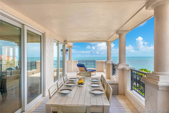 Balcony view of the ocean from a luxury apartment, featuring a dining table and lounge chair.