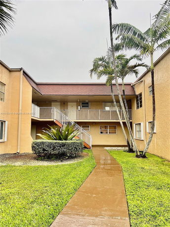 Front view of a two-story apartment building with balconies and palm trees.