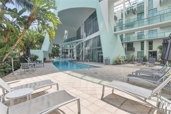 Outdoor swimming pool area adjacent to a modern building with glass balconies.