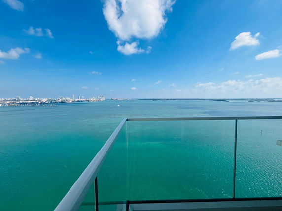 View from a balcony overlooking the ocean and distant city skyline.