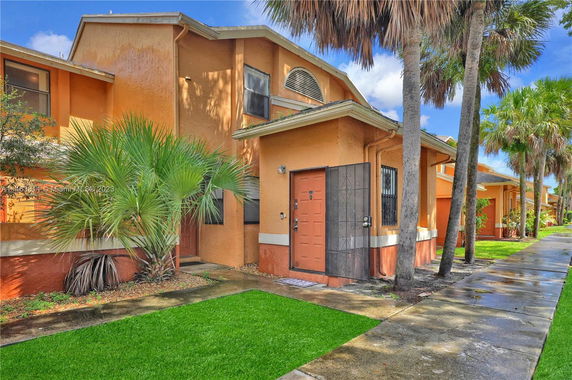 Front view of a two-story house with a pathway and palm trees.