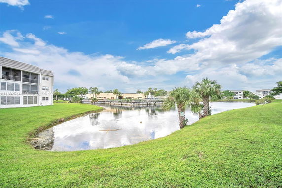 View of a building next to a small lake surrounded by grass and palm trees.