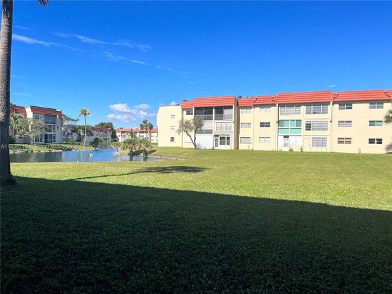 View of multiple apartment buildings with a grassy area and small pond.