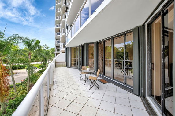 Outdoor balcony view of a modern building with large glass windows and surrounding palm trees.