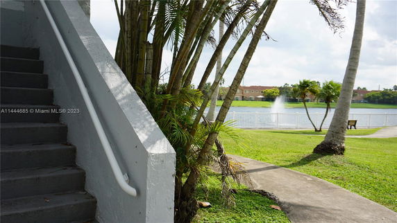 Outdoor scene with a staircase, palm trees, and a view of a lake with a fountain.