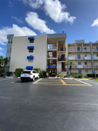 Front view of a multi-story building with balconies and a parking area.