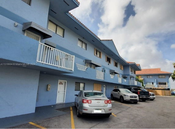 Front view of a multi-story building with balconies and a parking area.