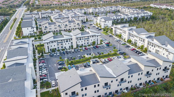 Aerial view of a residential complex with multiple modern white buildings and adjacent parking spaces.