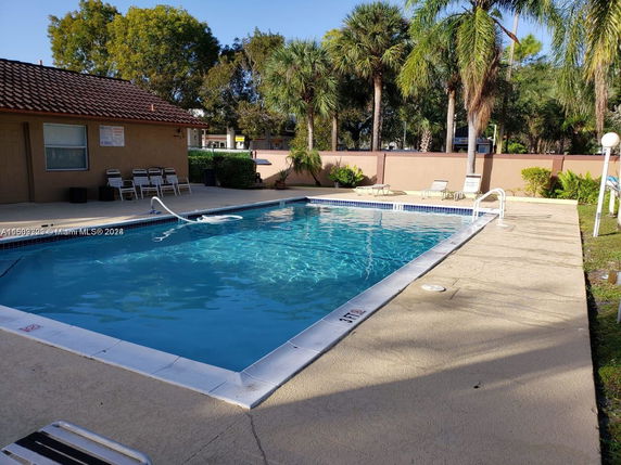 Outdoor swimming pool area with lounge chairs and a small building nearby.