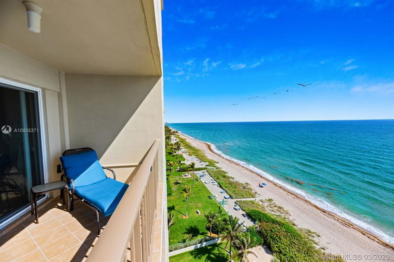 Panoramic view from a balcony overlooking the ocean and a sandy beach.
