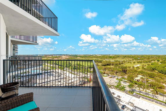 View from a balcony overlooking a scenic landscape with palm trees and distant buildings.