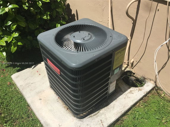 Outdoor air conditioning unit on a concrete pad next to a building wall.