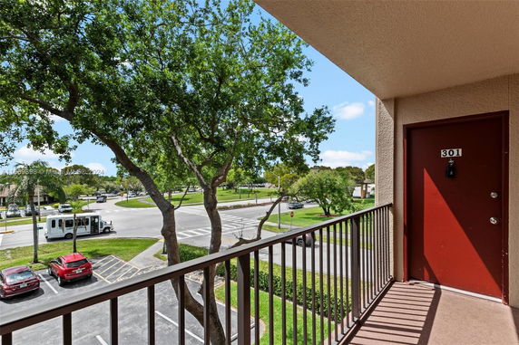 View from a balcony showing a parking area and street with trees and vehicles.