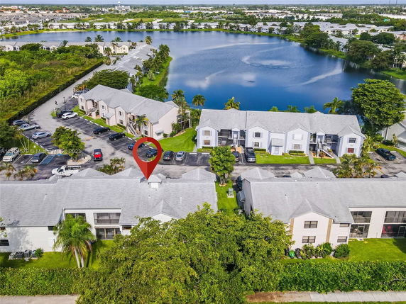 Aerial view of residential buildings near a lake with parking areas and greenery.
