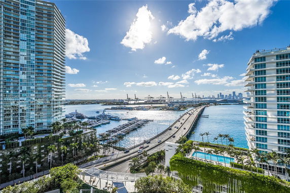 Panoramic view of waterfront buildings and a bridge, with a marina and city skyline in the background.