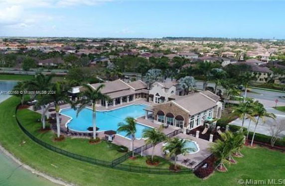 Aerial view of a large recreational building with a swimming pool surrounded by palm trees.