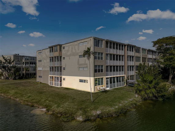 Front view of a multi-story residential building with several balconies and windows, situated by a water body.