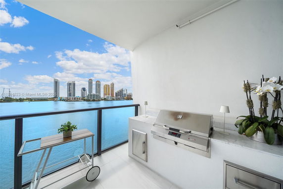 Balcony view with outdoor grill and modern high-rise buildings across the water.