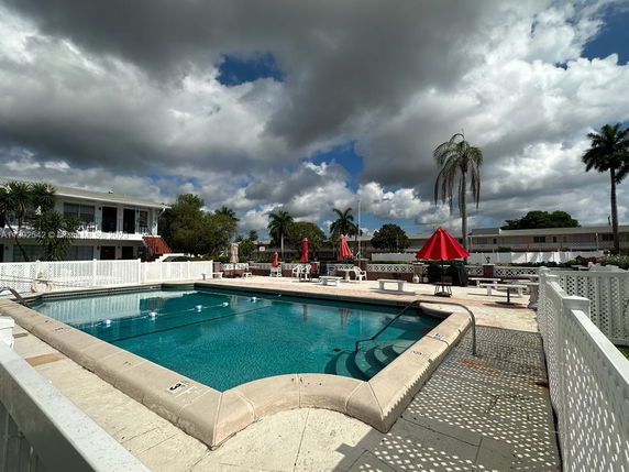 Outdoor swimming pool area with a two-story building in the background.