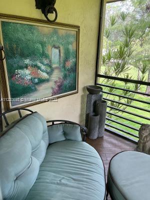 Patio area with outdoor seating, artwork on the wall, and a view of greenery through the railing.
