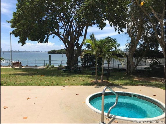 View of a backyard with a small pool, trees, and a waterfront in the background.