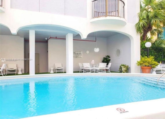 Outdoor swimming pool area with chairs and tables under archway.