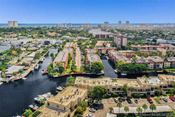 Aerial view of a coastal cityscape with waterways, residential buildings, and a distant ocean.