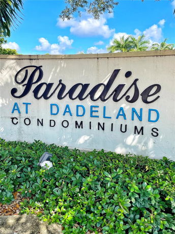 Sign reading 'Paradise at Dadeland Condominiums' with greenery and blue sky in the background.