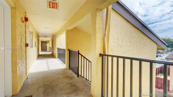 Exterior corridor of a building with yellow walls and an exit sign.
