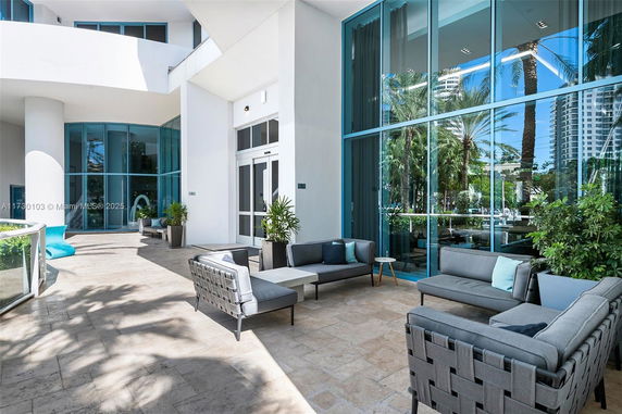 Outdoor seating area adjacent to modern building with large glass windows and potted plants.