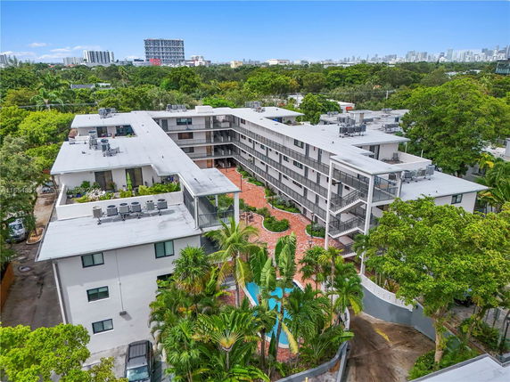 Aerial view of a multi-story residential building surrounded by trees and cityscape in the distance.