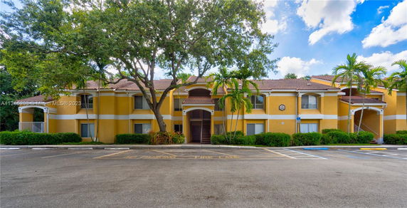 Front view of a two-story yellow building with a tiled roof and surrounding palm trees.
