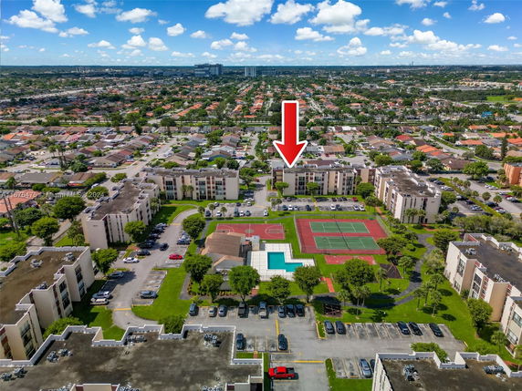 Aerial view of residential buildings with a tennis court and swimming pool among surrounding areas.