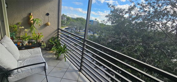 View from a balcony with outdoor plants and railing, overlooking trees and buildings.