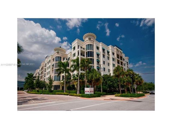 Front view of a multi-story apartment building with large windows and palm trees.