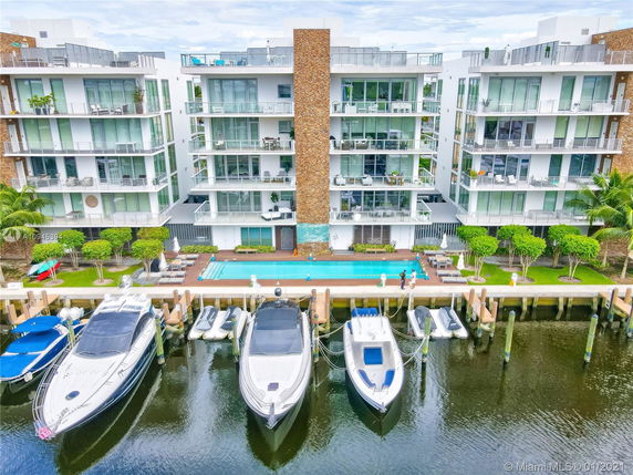 Front view of a modern multi-story apartment building with large glass balconies, facing a waterway.