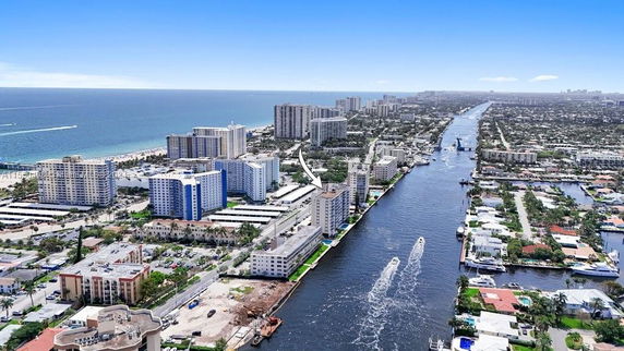 Aerial view of a coastal city with high-rise buildings, waterways, and a distant view of the ocean.
