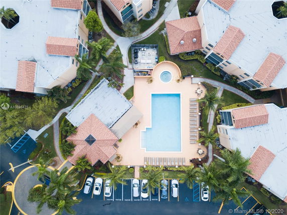 Aerial view of a swimming pool surrounded by residential buildings with parking area and landscaped paths.