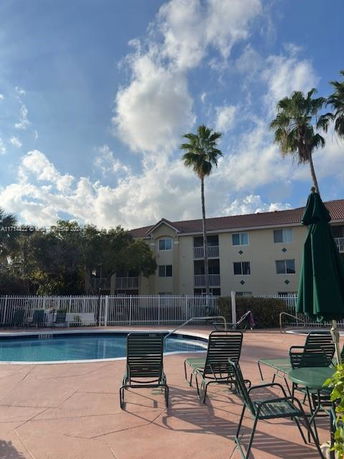 Swimming pool area with loungers in front of a multi-story residential building.