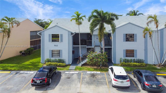 Front view of a two-story residential building with balcony and palm trees.