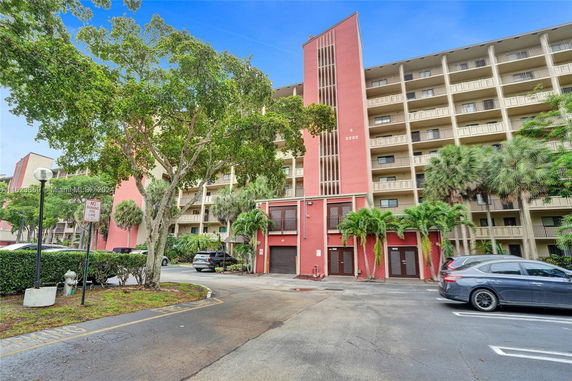 Front view of a multi-story residential building with balconies and a parking area.