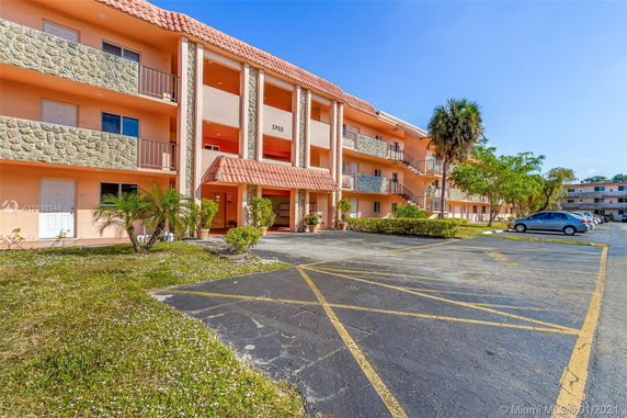 Front view of a multi-story apartment building with balconies and a parking area.
