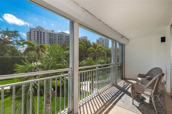Outdoor balcony with wicker chairs overlooking a lush green area and distant view of tall buildings.