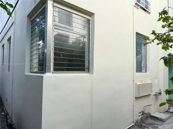 Corner view of a building with louvered windows and an external air conditioning unit.