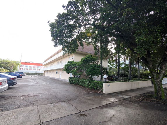 Outdoor parking area beside a multi-story building with trees and cars parked.