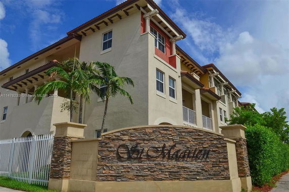 Front view of a multi-story building with a stone and stucco facade, featuring balconies and a decorative sign.