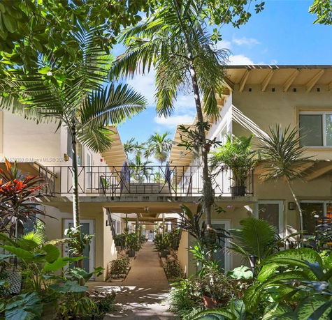 Front view of a two-story building with balconies and tropical plants.