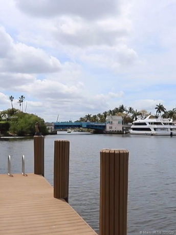 View of a waterway with a wooden dock, a yacht, and a blue bridge in the background.