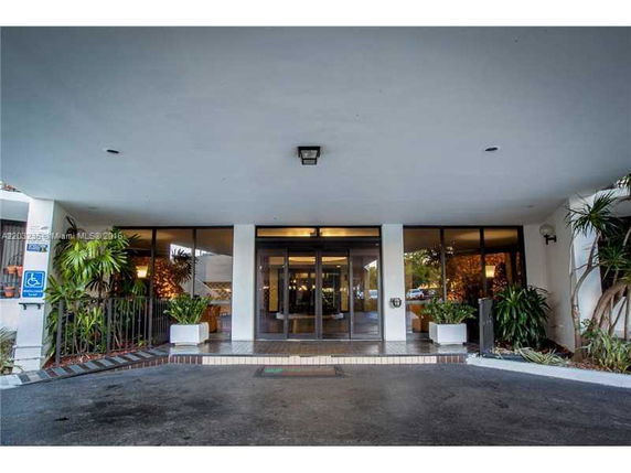 Entrance to a building with large glass doors and plants on either side.